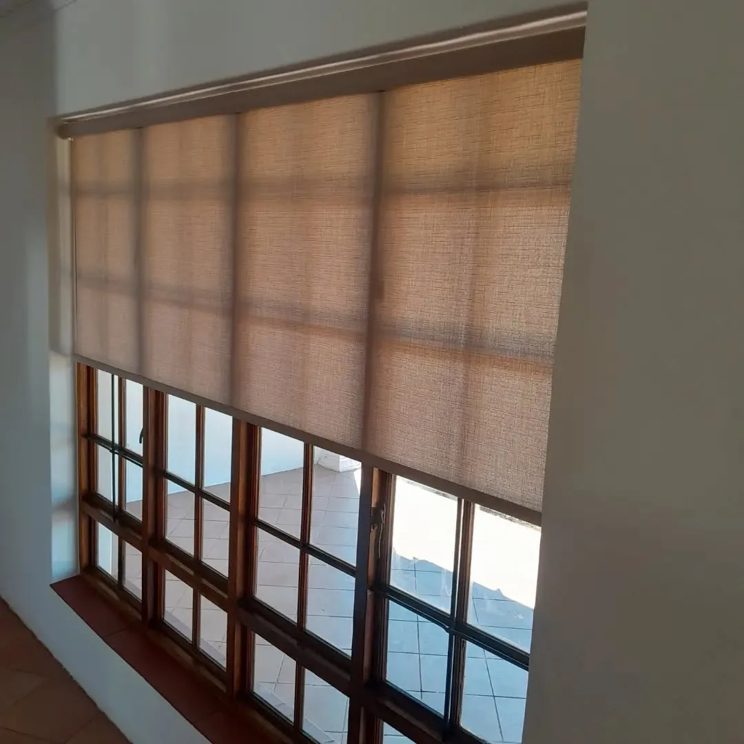 Sunscreen roller blind fitted to a corner window over a wooden window sill