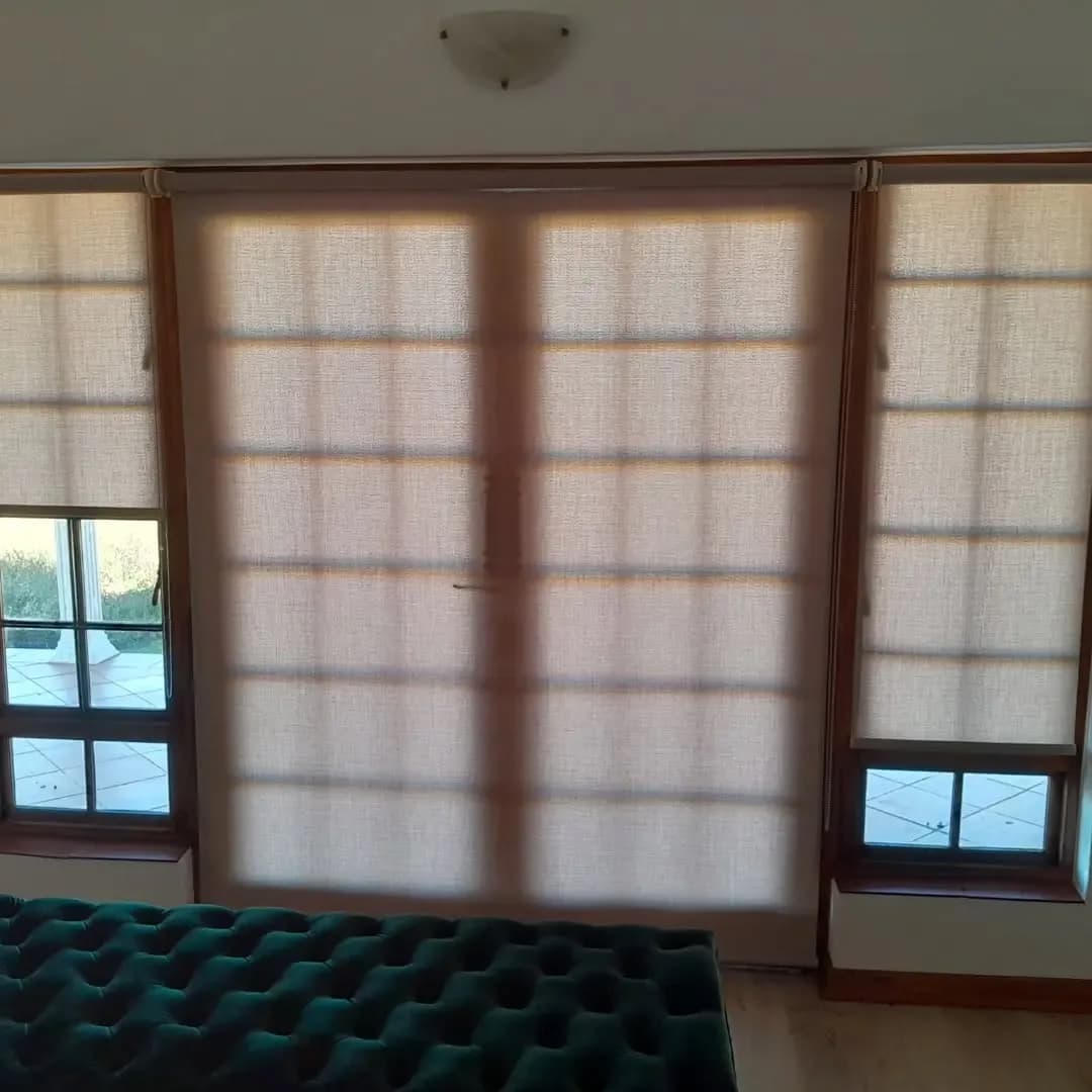 Sunscreen roller blinds fitted across a patio door and side windows in a bedroom